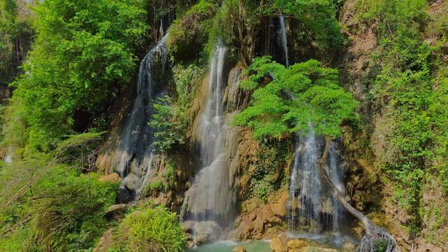 Aerial view of Sri Gethuk Waterfall cascading down rocky cliffs surrounded by lush green tropical forest and foliage in Yogyakarta, Special Region of Yogyakarta, Indonesia.