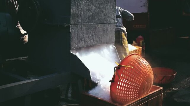 An industrial ice machine dispenses crushed ice into a red plastic basket, used for cooling and preserving fresh produce or seafood in an Indian market.
