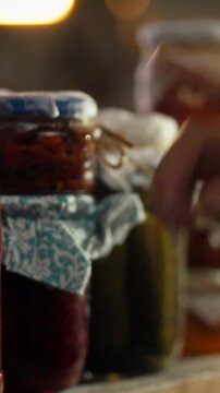 Man's hand pulls glass jar from wooden shelf in dim, cool cellar, where rows of fermented food sit, metal handles on the shelf and low lighting provide food preservation and healthy eating practices
