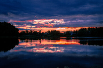Obraz premium Dramatic dark blue twilight sky with glowing orange sunset slit reflected on lake