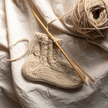 Knitting in progress with wool socks and needles on linen cozy flat lay