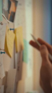 Man in glasses stands beside a wall-mounted whiteboard, arranging sticky notes to map business strategy and planning, organizing complex tasks in an educational environment focused on problem-solving