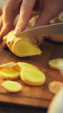 Man in a kitchen chops fresh ginger rhizome on a cutting board, the pungent aroma filling the air as he prepares food, a culinary preparation for a healthy morning drink, showing the cooking process