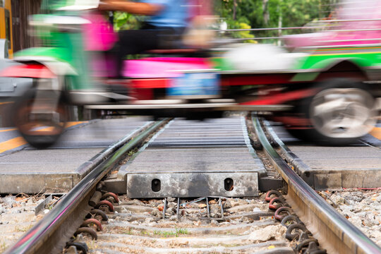 Motion blur shot of a green motorcycle with a sidecar speeding across a railroad level crossing in Thailand, showing close-up steel railway tracks and ballast ground.
