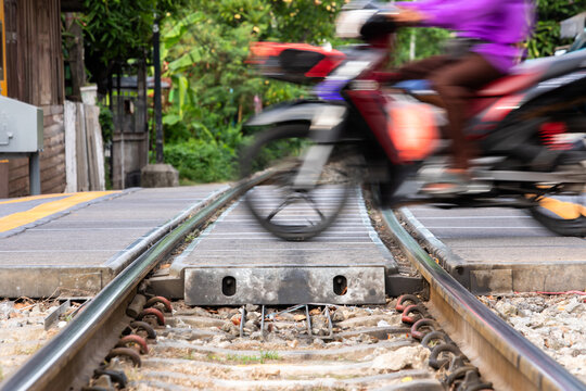 Motion blur shot of a motorcycle riding quickly across a railroad level crossing, showing close-up railway tracks, steel rails, and road infrastructure in Thailand.