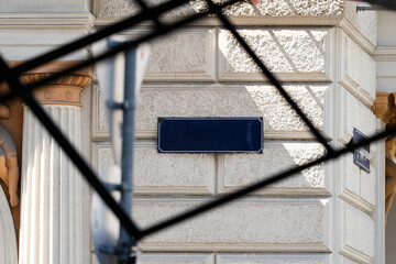 Plaque decorates facade. Architecture frames plaque. Scaffolding crosses building. Stonework creates texture. Ornate stone blocks, dark blue plaque, metal framework, classical details create © VladyslavShcherbakov