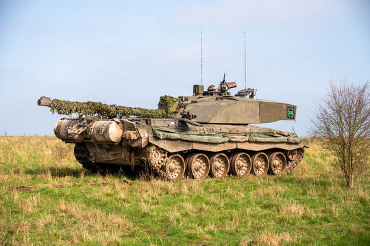 View of a British Challenger 2 main battle tank with camouflage netting on its gun barrel parked on the grassy terrain of Salisbury Plain in Salisbury, Wiltshire, United Kingdom.