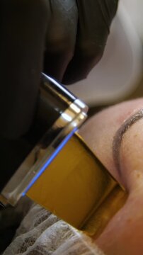 Professional beautician applying cleansing mask on female client's face. Close-up of female face during youth restoration and facial rejuvenation procedure  - Vertical Video
