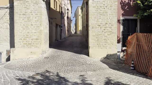 Uno scorcio di un antico borgo italiano con un vicolo in ciottoli che si snoda tra storici edifici in pietra e mura storiche sotto la luce del sole