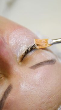 Professional beautician applying cleansing mask on female client's face. Close-up of female face during youth restoration and facial rejuvenation procedure  - Vertical Video