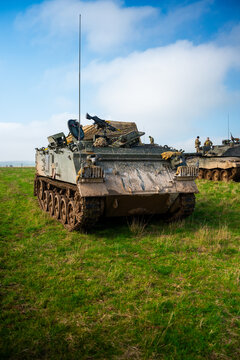 View of British Army armoured vehicles and tanks stationed on the grassy terrain of Salisbury Plain with soldiers standing nearby in Salisbury, Wilshire, United Kingdom.