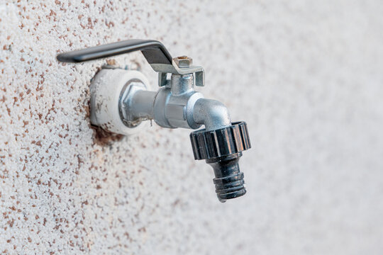 metal outdoor faucet with hose connector mounted on a textured stucco exterior wall, showing signs of age and use. Maintenance concept.