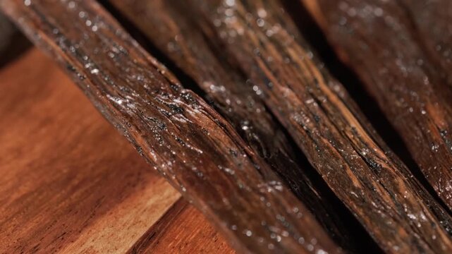 Cinematic macro close-up featuring an upward panning motion across vanilla bean pods placed over a knife and wooden cutting board. Warm lighting and shallow depth of field highlight their rich texture