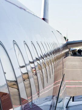 View of the reflective fuselage and row of windows of a commercial airplane parked on the tarmac at Amsterdam, North Holland, Netherlands.