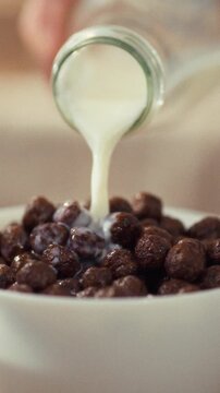 In a warm kitchen, a person pours fresh milk over chocolate cereal, creating a breakfast scene where ingredients are prepared for a calm, quiet morning, a simple act of serving a meal