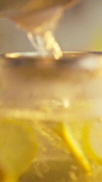 In a kitchen, a glass teapot containing lemon slices and ginger receives a stream of boiling water, infusing the beverage, the mixture releases citrus aroma and creates a textured, warm drink