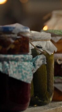 In a dimly lit basement, a hand places a jar of homemade pickles onto a wooden shelf, while the owner carries organic preserve jars down stairs, showing a food storage routine rooted in agriculture