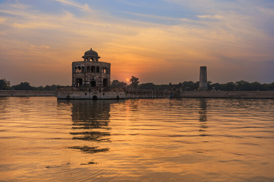 View of Hiran Minar pavilion reflected in the surrounding water during a golden sunset in Sheikhupura, Punjab, Pakistan.