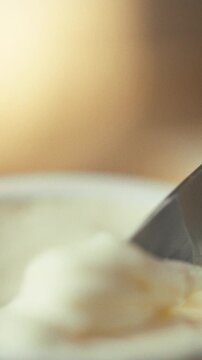 Hand carefully unwraps store-bought block cream cheese from its plastic packaging using knife, preparing it for spreading, altering its texture, in process food preparation involving dairy products