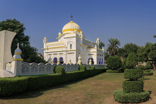 View of Gurdwara Mal Ji Sahib with its yellow dome, white walls, and manicured hedges in a peaceful garden setting in Nankana Sahib, Punjab, Pakistan.