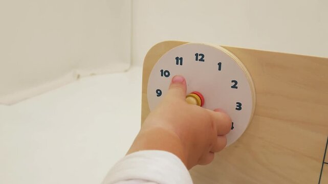 Toddler hand pointing at a toy clock face on a wooden activity bench at home. Early education