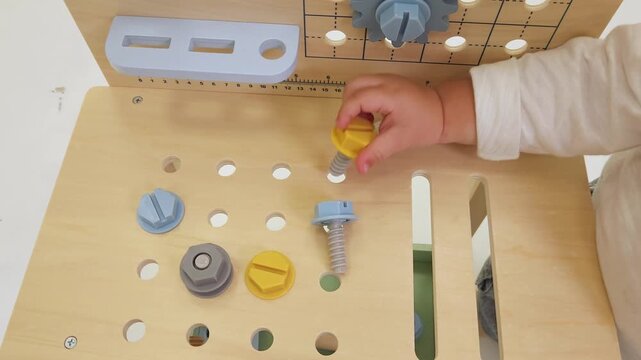 High angle shot of child hand turning yellow bolt on wooden activity table. Early education