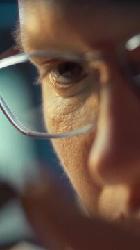 Close-up of a man wearing glasses works intently in a workshop, carefully analyzing small parts metal tools lie on a workbench in dim lighting as he examines the details