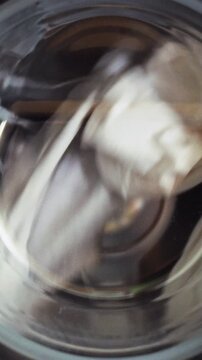Clean laundry is visible through transparent window as a front-loading washing machine's drum rotates, starting a thorough clothes cleaning cycle, part of household housework and daily appliance use