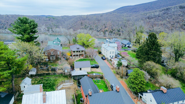 Residential asphalt lane crosses Washington Street neighborhood toward Potomac River shoreline. Forested mountain slopes border historic residential enclave in Harpers Ferry, West Virginia