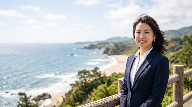 プロフィール写真をイメージした、夏の海岸を背にして爽やかな風に吹かれている、穏やかな笑顔をカメラに向けている知的な印象の20代日本人女性社員のバストアップポートレート