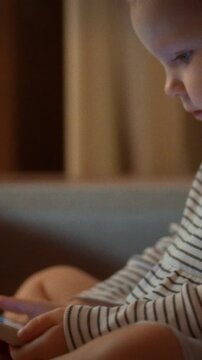 A toddler sits on a sofa, eyes fixed on a smartphone's bright screen showing colorful images in a quiet evening, a childcare setting with prolonged screen time in a home environment
