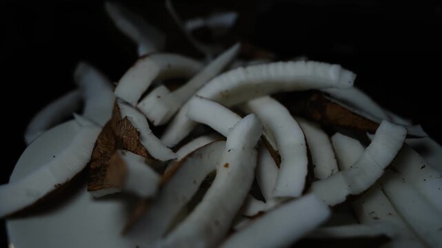 Close up of sliced coconut pieces with white flesh and brown shell on a dark background