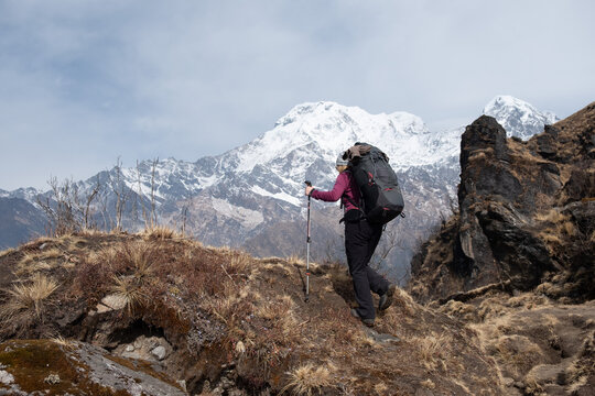 Eine Frau mit gro&szlig;em Rucksack steigt einen Bergpfad empor und erblickt das Bergpanorama der Annapurna Bergkette im Himalaya