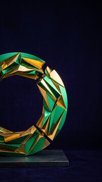 Geometric sculpture with green and gold faceted surfaces on a dark background, showcasing modern art and abstract design