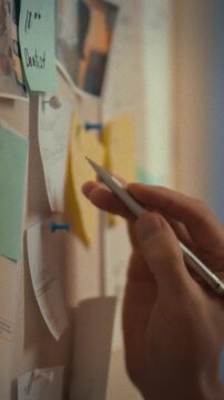 A man's hand arranges tasks on an indoor wall lined with bright sticky notes during work hours, part of business planning and organization, pinning each note to manage tasks efficiently