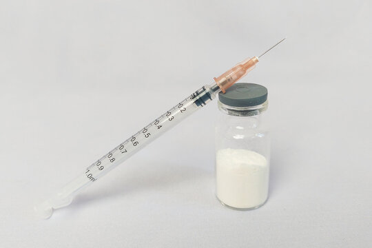 A syringe and a 100ml glass bottle containing crystal methamphetamine, white background.