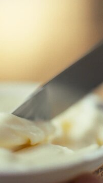 A hand carefully grasps a knife to extract a block of thick cream cheese from its store-bought packaging, preparing the dairy product for spreading in a food prep setting during a kitchen routine