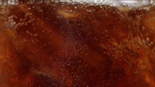 4K Extreme close-up macro shot of sparkling bubbles and ice cubes in cold brown cola drink, refreshing summer beverage, fizzy drink, cold refreshment and abstract texture.