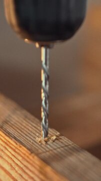 A carpenter works in a well-equipped workshop, operating an electric drill to bore a precise hole in a wood specimen, part of carpentry and woodworking processes in the industry