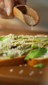 A chef's skilled hands sprinkle sesame seeds onto a breakfast sandwich in a quiet, cozy kitchen, a culinary step that adds nutritional value and flavor, part of a healthy morning routine
