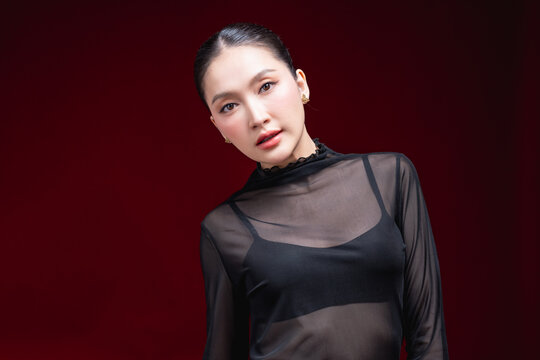 Side-profile beauty portrait of a young Asian woman in a sheer black top looking off to the side with a subtle expression against a deep red background.