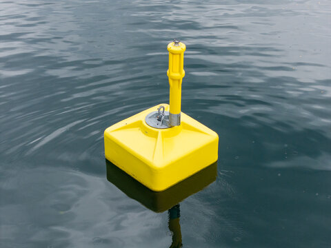 View of a bright yellow square buoy floating on the calm dark water of a fjord in Liabygda, More og Romsdal, Norway.