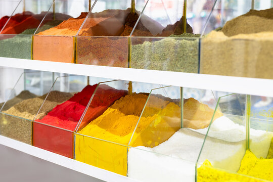 Colorful ground spices displayed in glass bins at an oriental bazaar in Bukhara. Vibrant rows of turmeric, paprika, and herbs on white shelves. Ideal for food background, travel content.