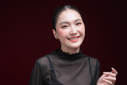 Dramatic close-up beauty portrait of a young Asian woman in a sheer black top gazing intensely at the camera against a deep red and black background.