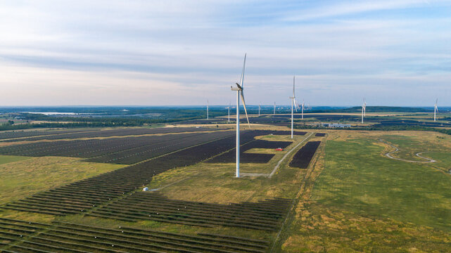Aerial view of a large hybrid power plant combining wind turbines and solar panels across a vast rural landscape in Poland.
