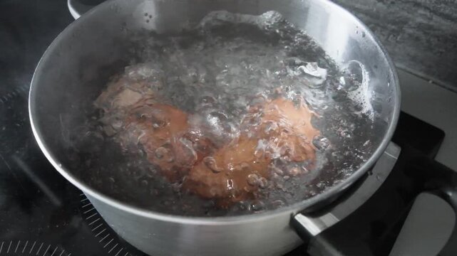 Eggs boiling in bubbling water inside a stainless steel pot