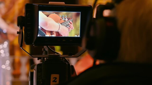 Professional cameraman filming performance of musician playing mandolin on stage at concert.