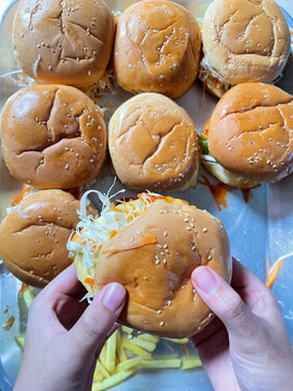 Fresh soft burger buns with sesame seeds displayed on a tray, with hands holding a bun filled with shredded vegetables.