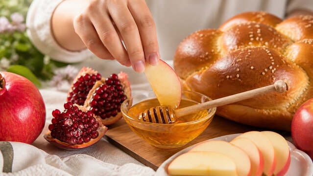Hand dipping an apple slice into honey for Rosh Hashanah