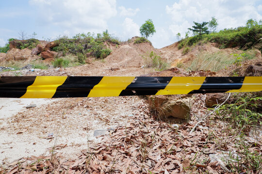 Yellow and black striped hazard caution tape stretched across a rocky terrain covered with dry leaves to block access. Ideal for editorial articles, safety presentations